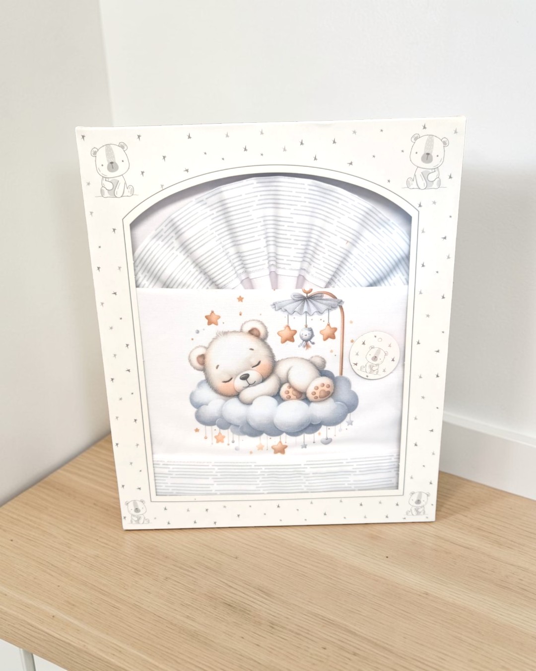 Caixa branca com padrão e desenho de urso e roupa de bebé com urso a dormir na nuvem.