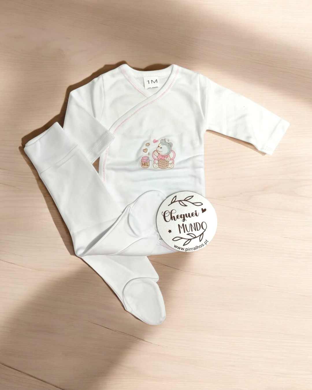 Conjunto de roupa branco para bebé com bordado de urso e etiqueta redonda sobre madeira clara
