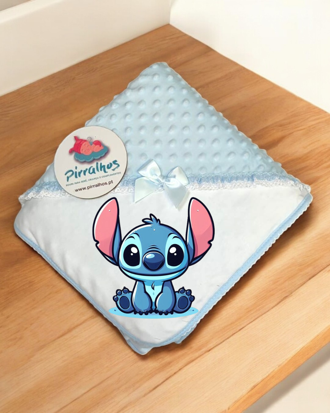 Manta de bebé azul com personagem Stitch e etiqueta Pirralhos sobre madeira
