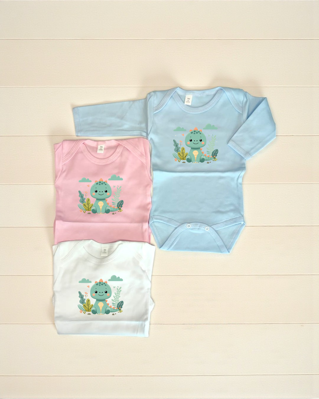 Três bodies de bebé azul, rosa e branco com estampa de dinossauro