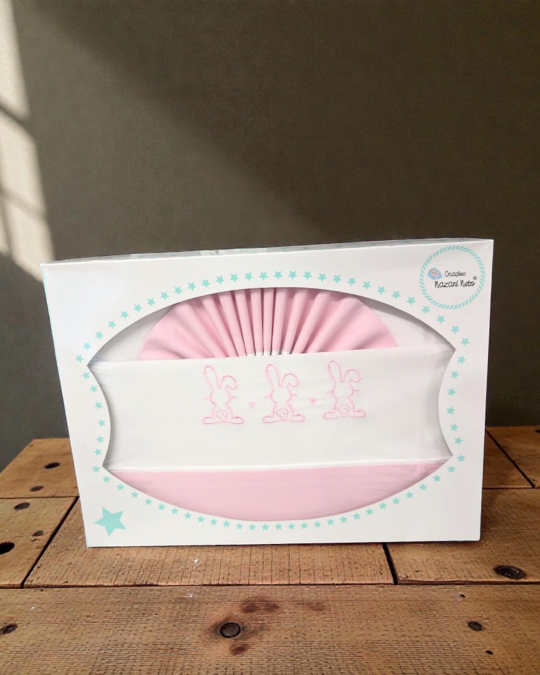 Roupa de bebé rosa e branca com bordado de coelhinhos numa caixa branca com estrelas.