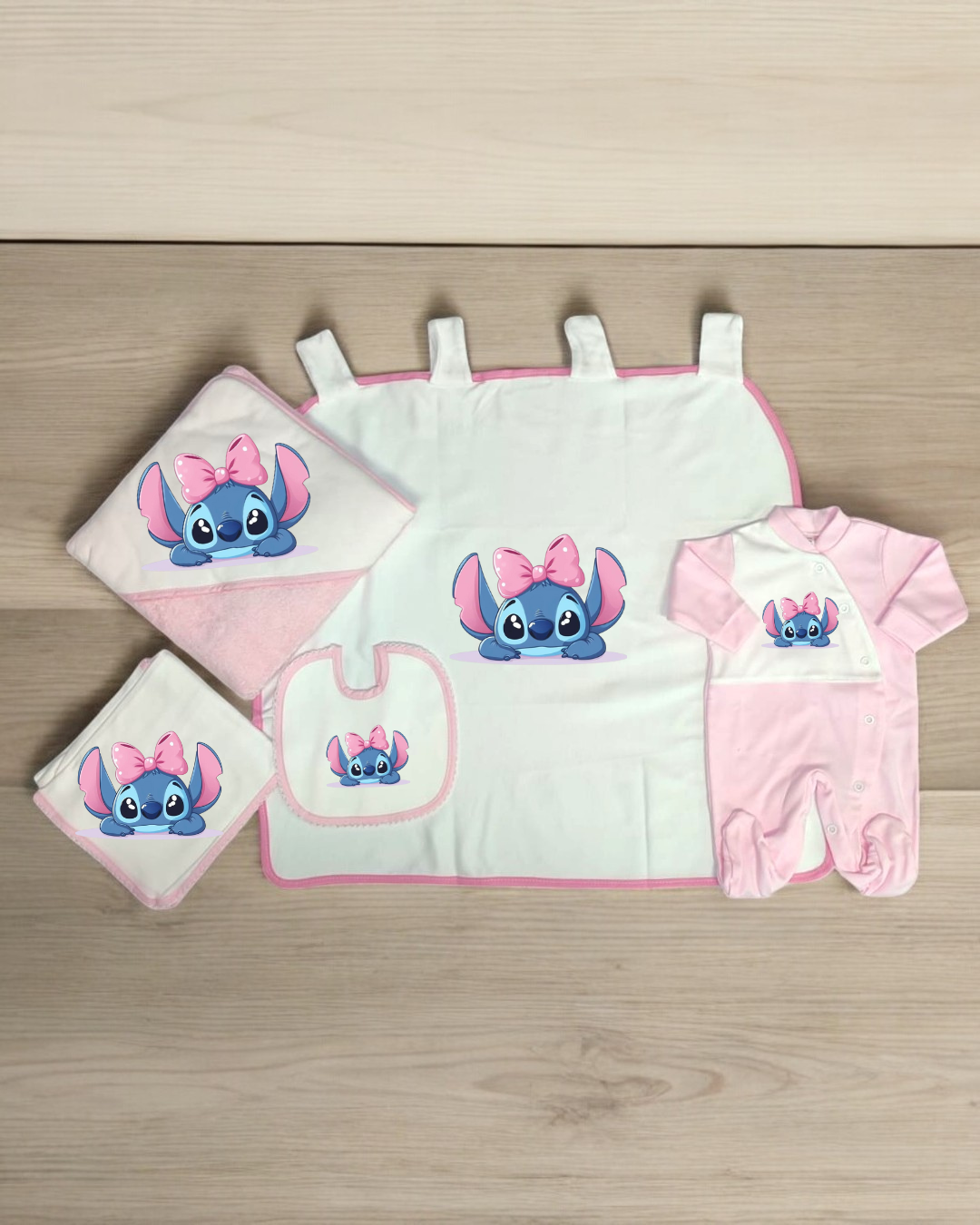 Conjunto de bebé com manta, babete, toalha e pijama com estampa de personagem azul e laço cor-de-rosa