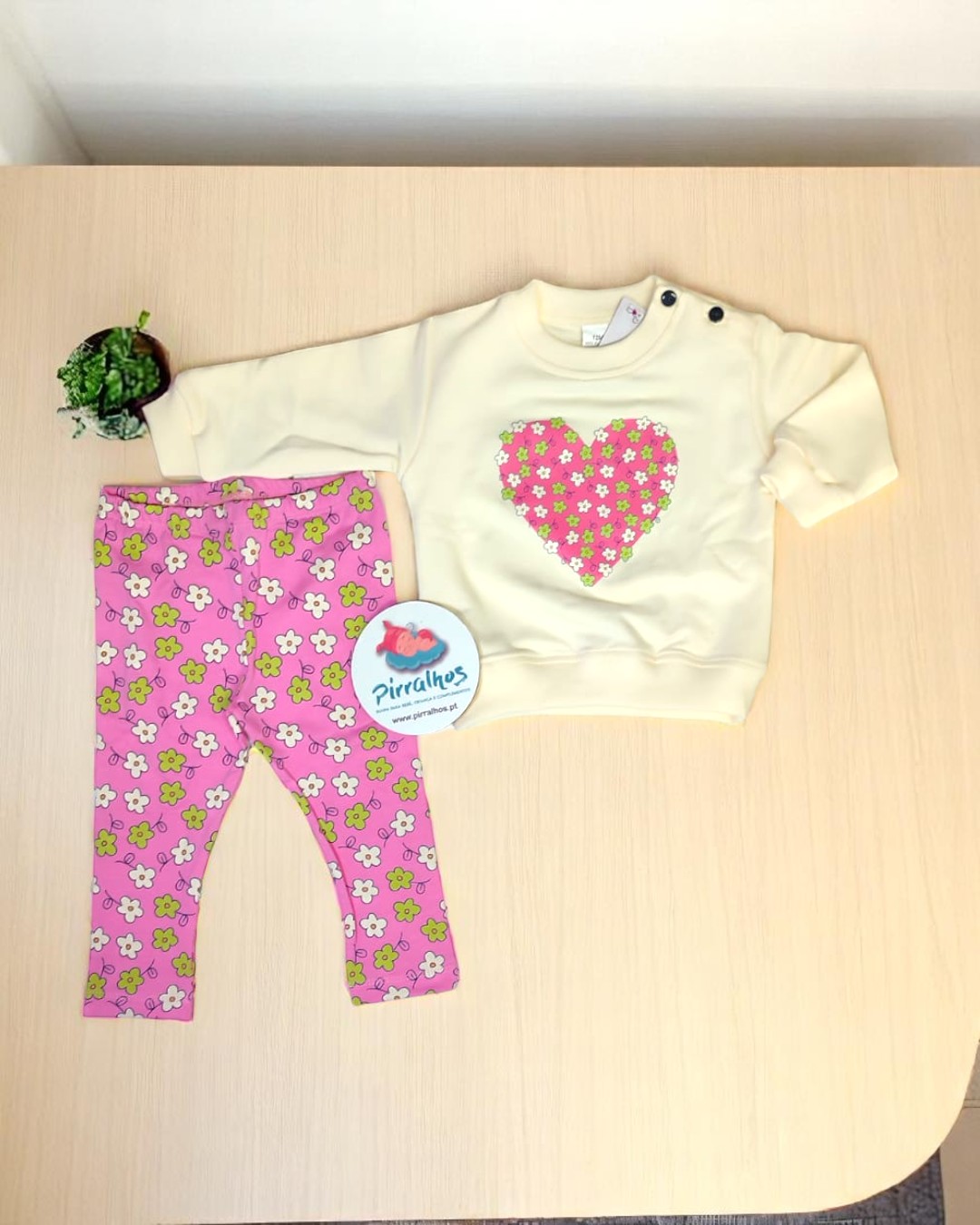 Conjunto infantil creme e rosa com padrão floral sobre mesa de madeira