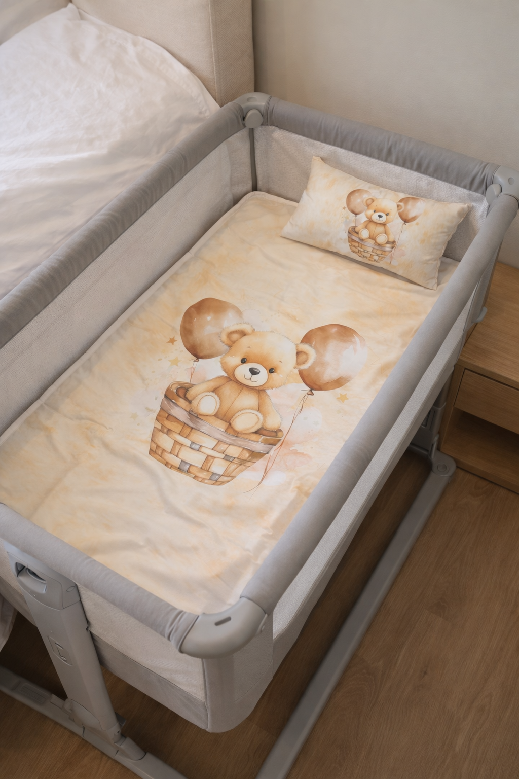 Berço portátil cinzento com colcha e almofada bege com desenho de urso castanho