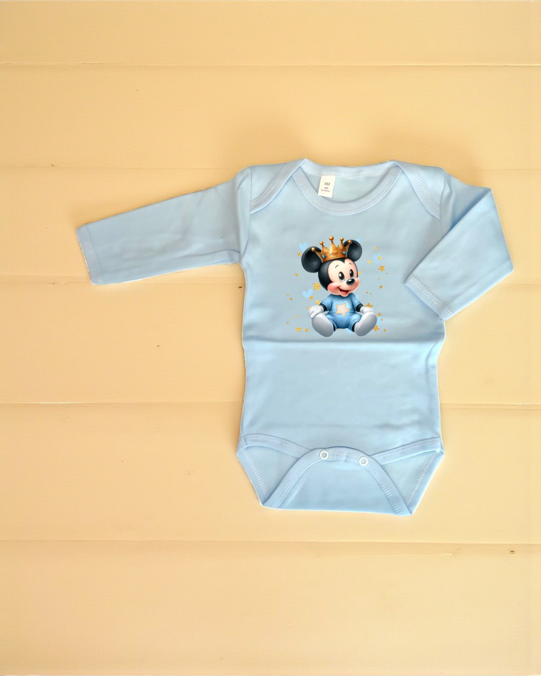 Body azul claro para bebé com estampa do Mickey Mouse bebé com coroa e fundo bege.