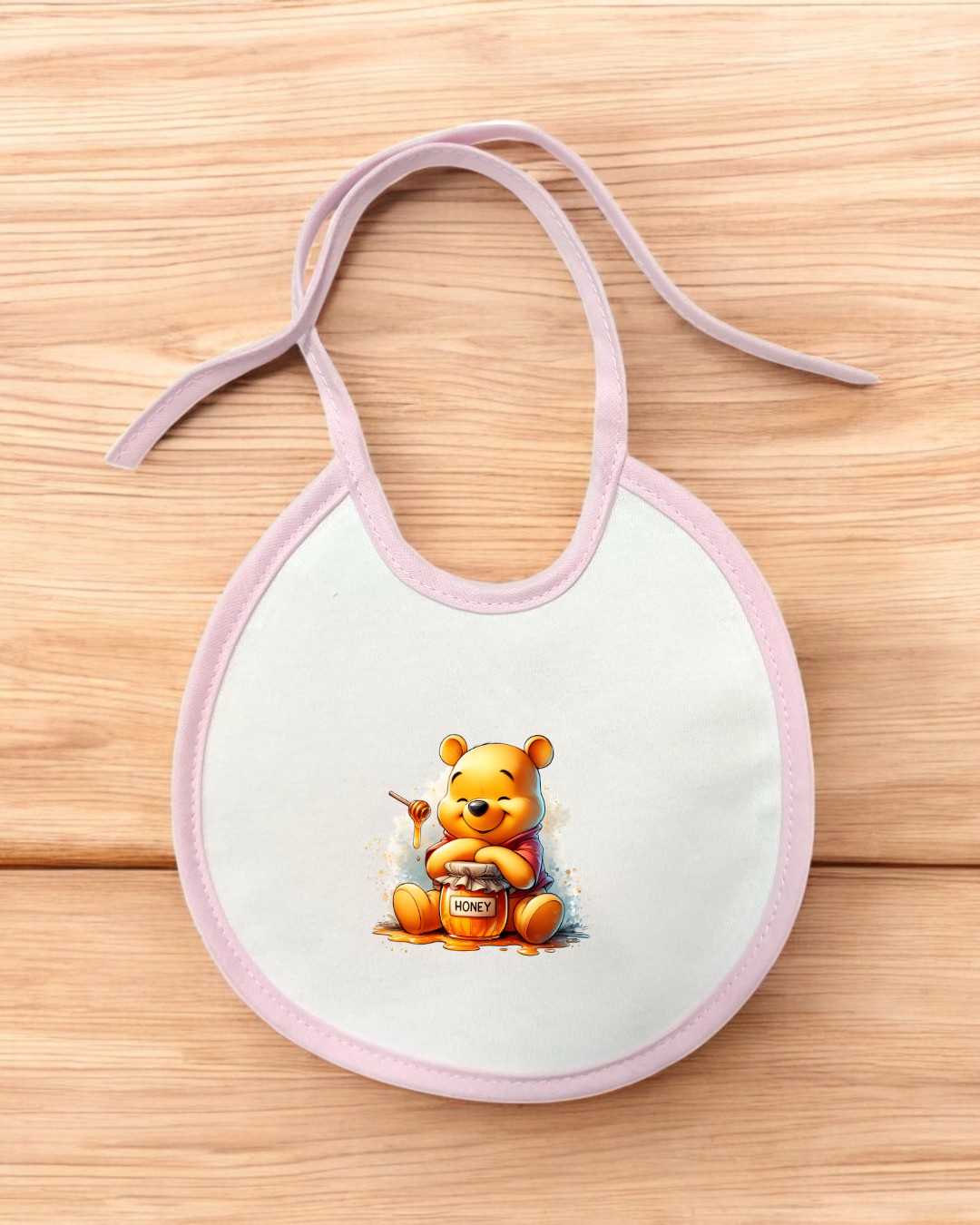 Babete branco com bordas lilás e desenho de urso amarelo segurando pote de mel