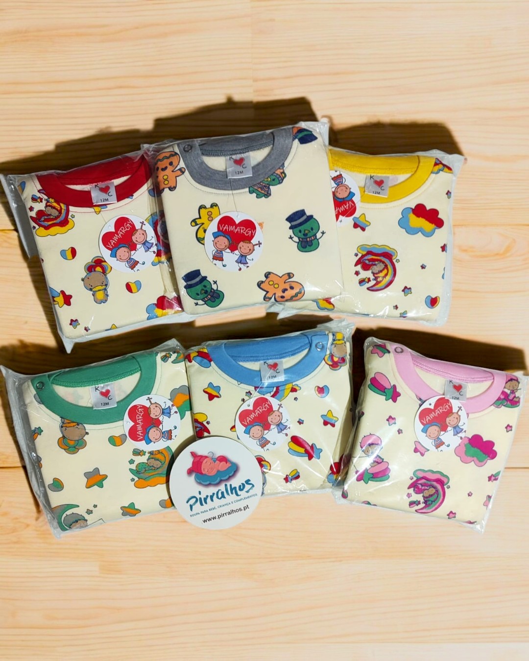 Conjuntos de roupa de bebé com estampados coloridos e golas de cores diferentes, embalados em plástico, sobre madeira clara