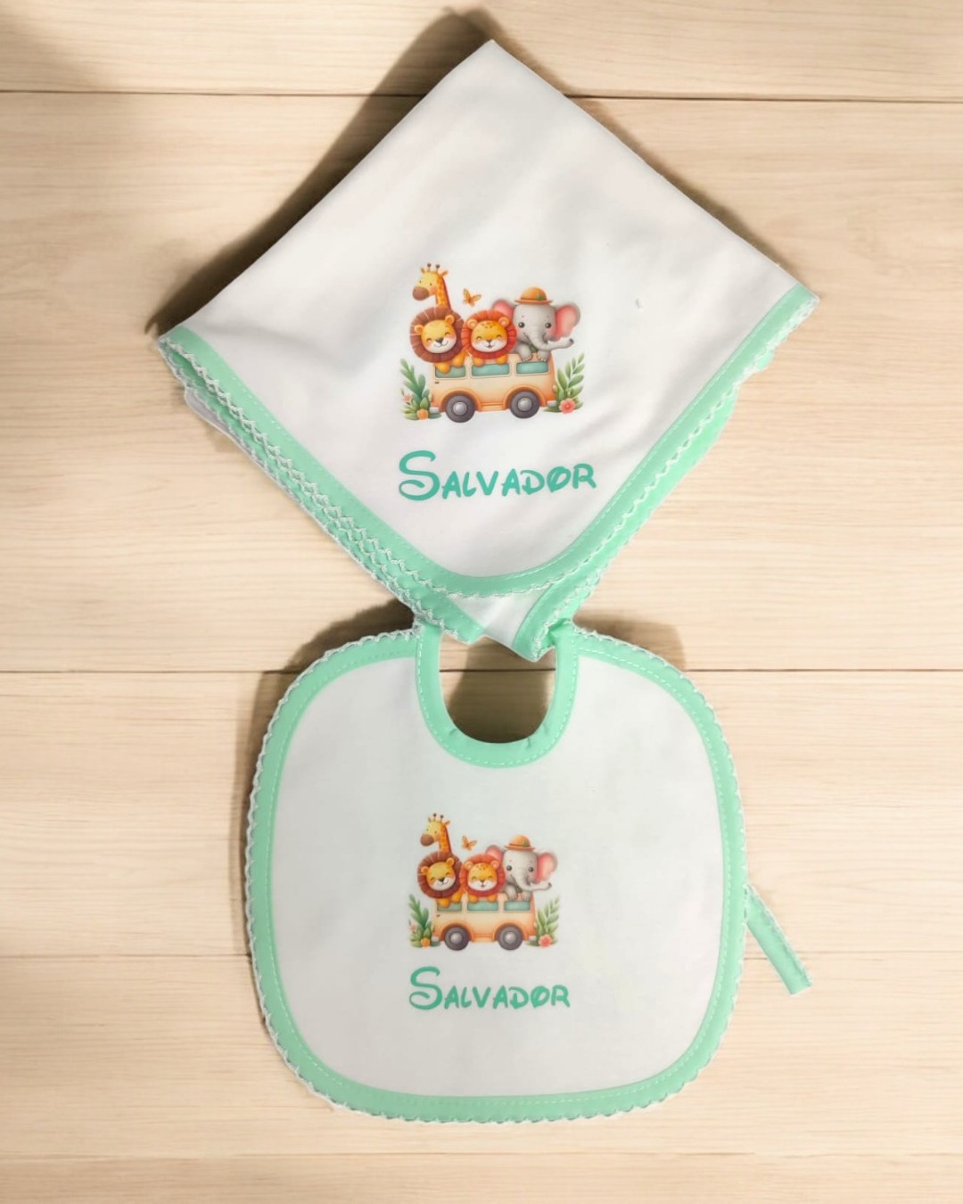 Babete e fralda brancos com bordas verdes e estampas de animais com o nome Salvador