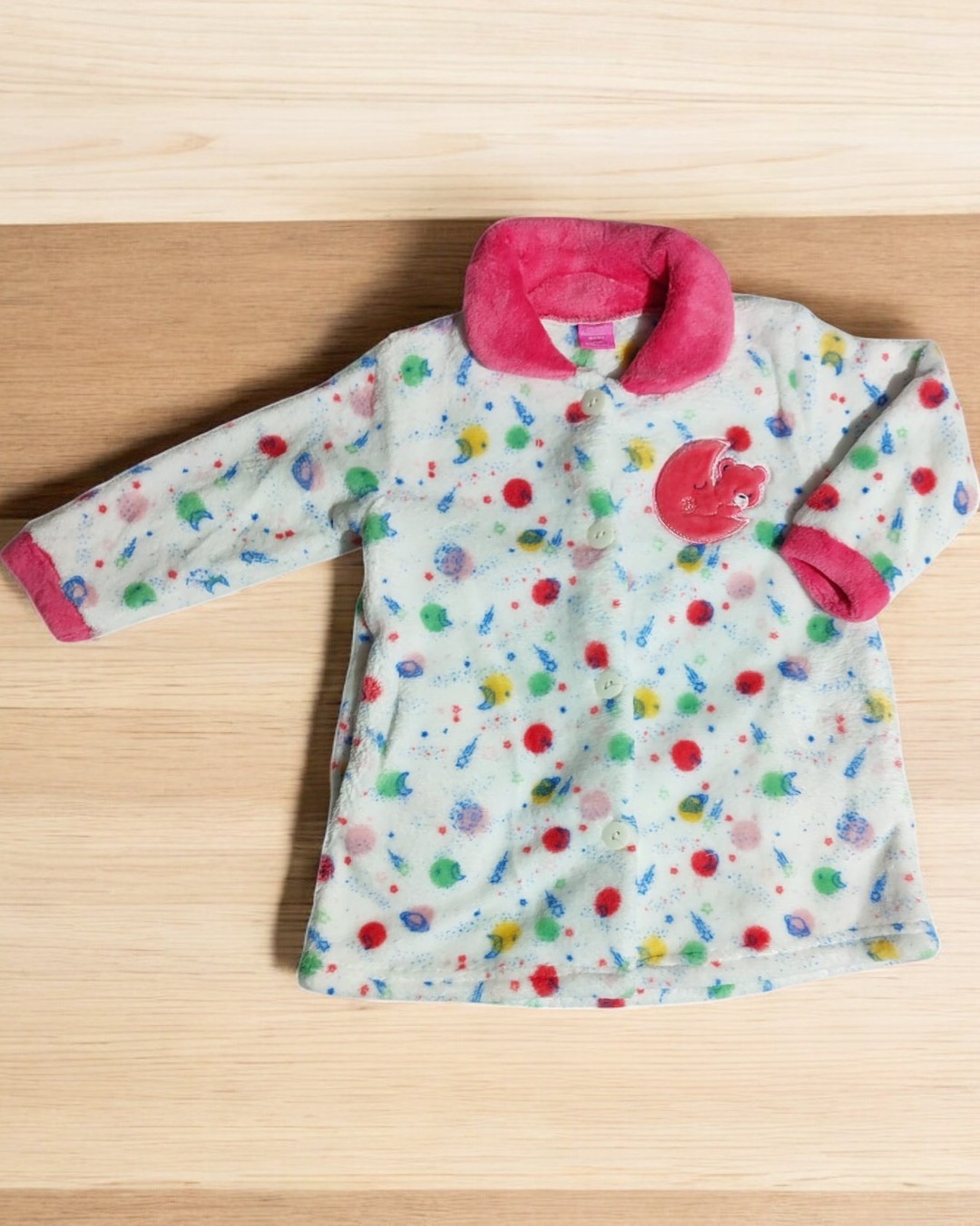 Casaco infantil branco com padrão colorido, gola e punhos rosa, aplique vermelho no peito