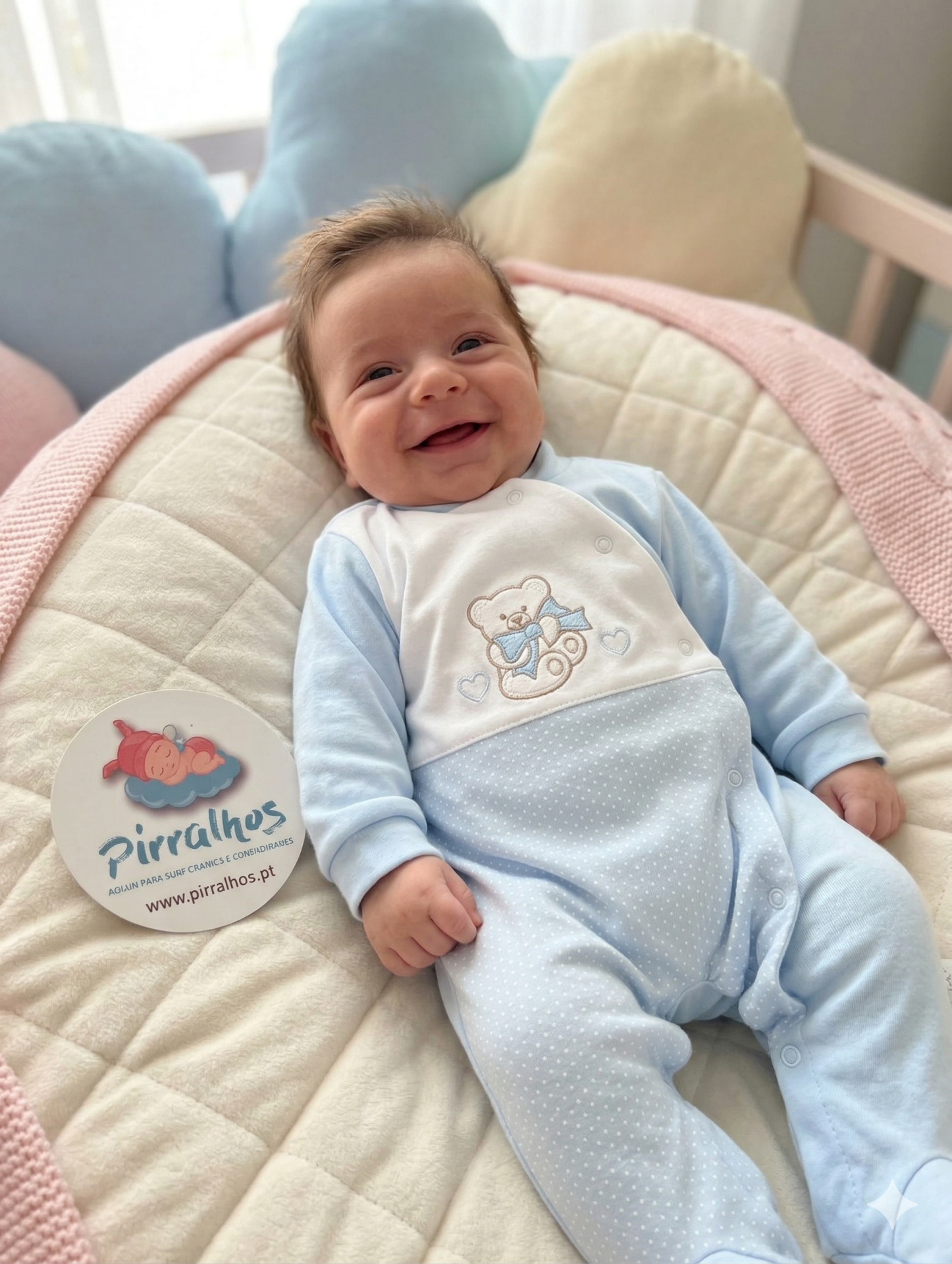 Bebé sorridente com babygrow azul claro e branco com bordado de ursinho.