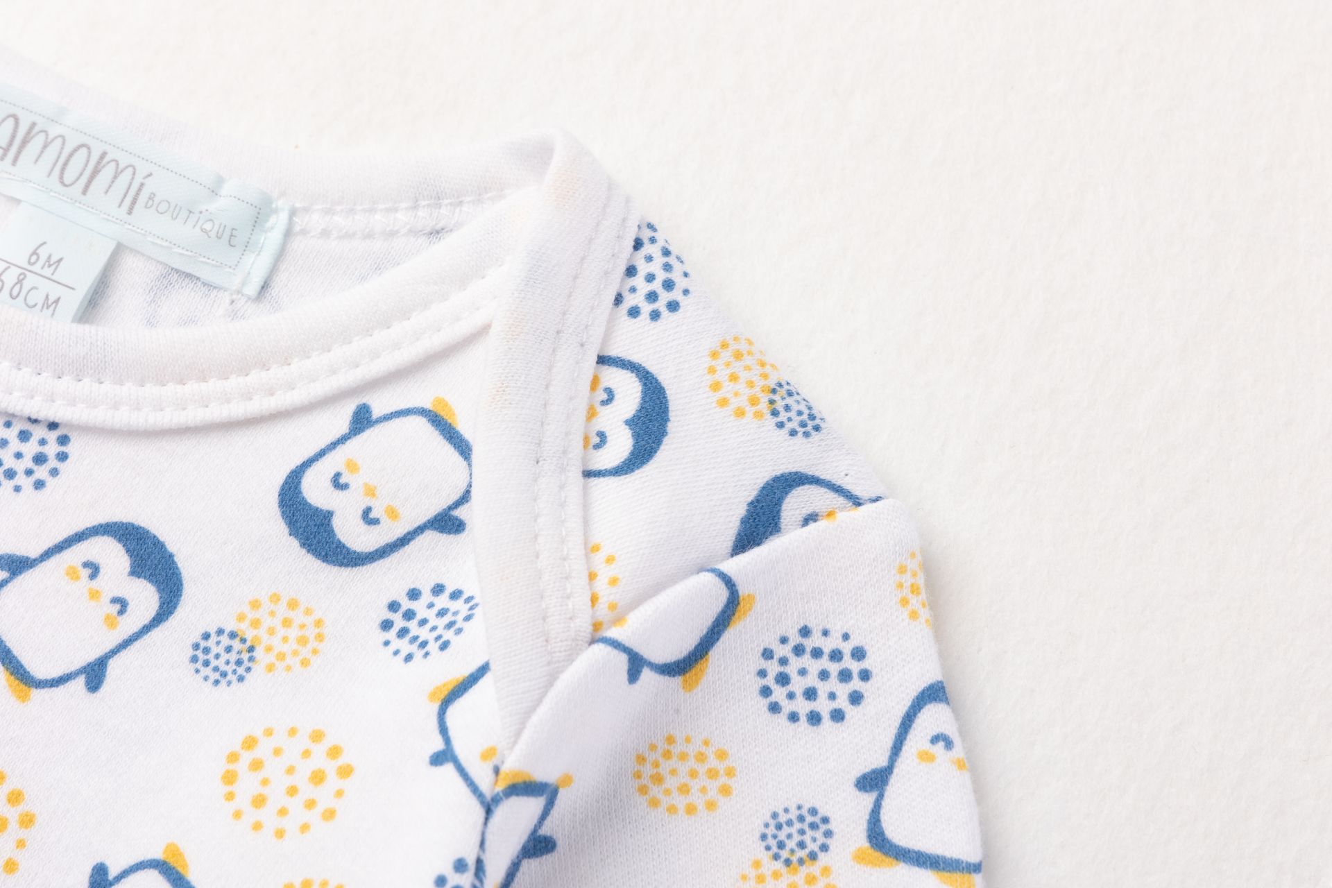 Roupa de bebé com estampado de pinguins azuis e amarelos em fundo branco