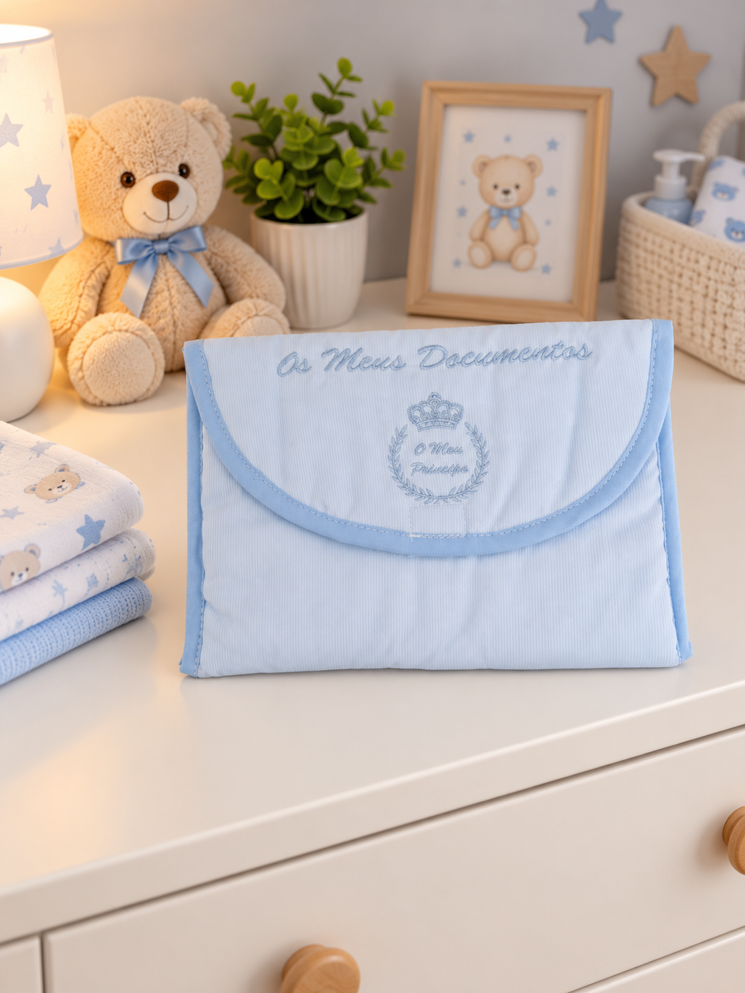 Bolsa azul clara para documentos de bebé com bordado em tom azul, em ambiente de quarto infantil com ursinho de peluche e fraldas.