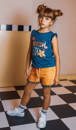 Menina com t-shirt azul, calções amarelos e sapatilhas brancas num chão xadrez preto e branco