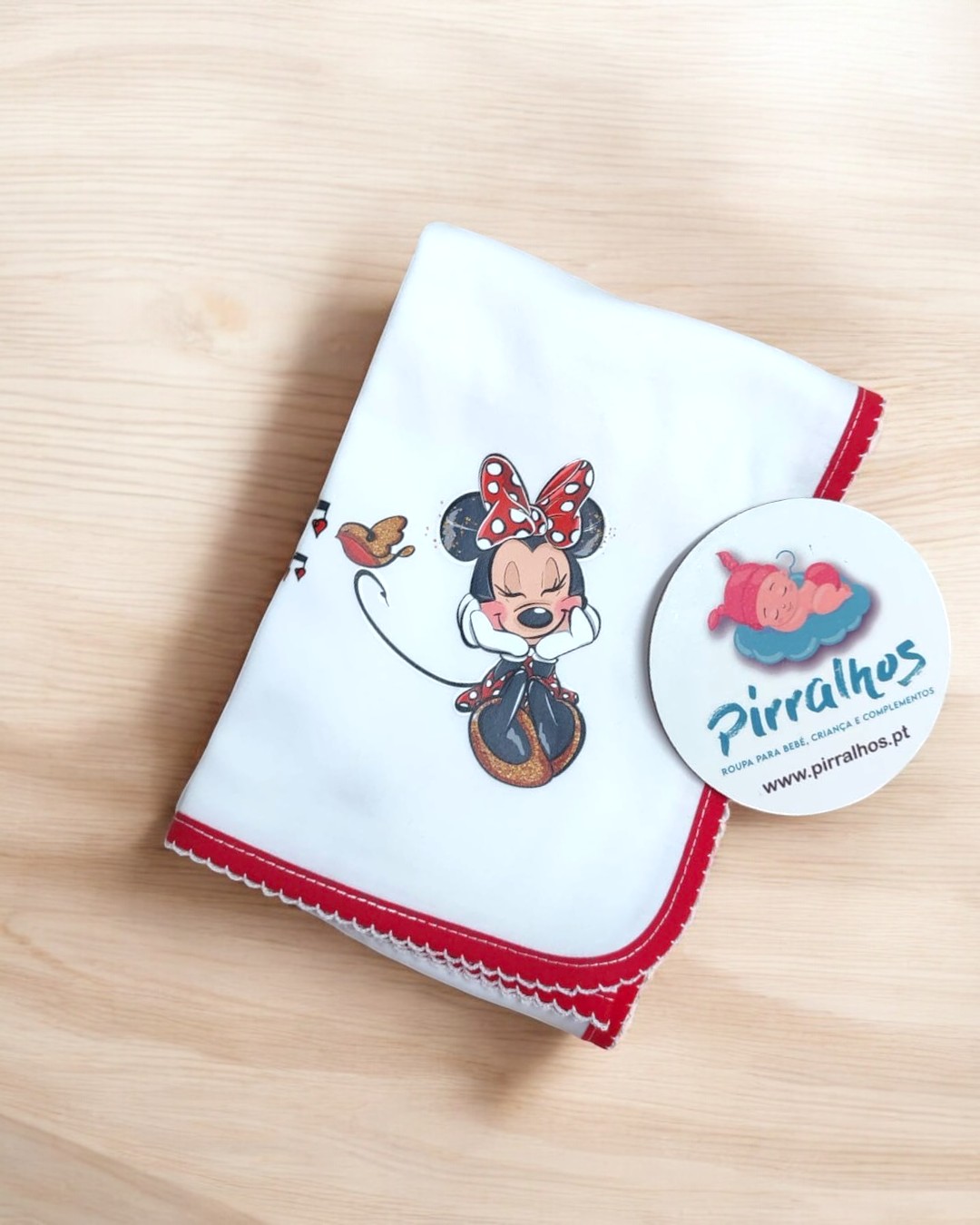 Fralda branca com bordadura vermelha e desenho da Minnie Mouse com pássaro, cartão com logo Pirralhos