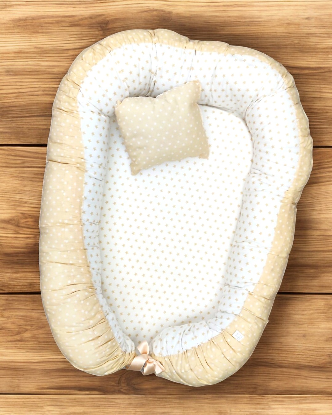 Cama de bebé oval bege e creme com estrelas pequenas e almofada quadrada