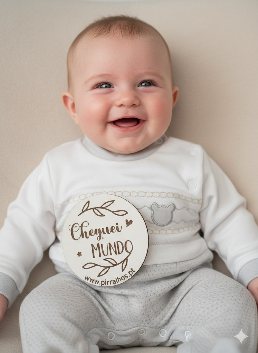 Bebé sorridente com roupa branca e cinza claro e placa de madeira Cheguei MUNDO