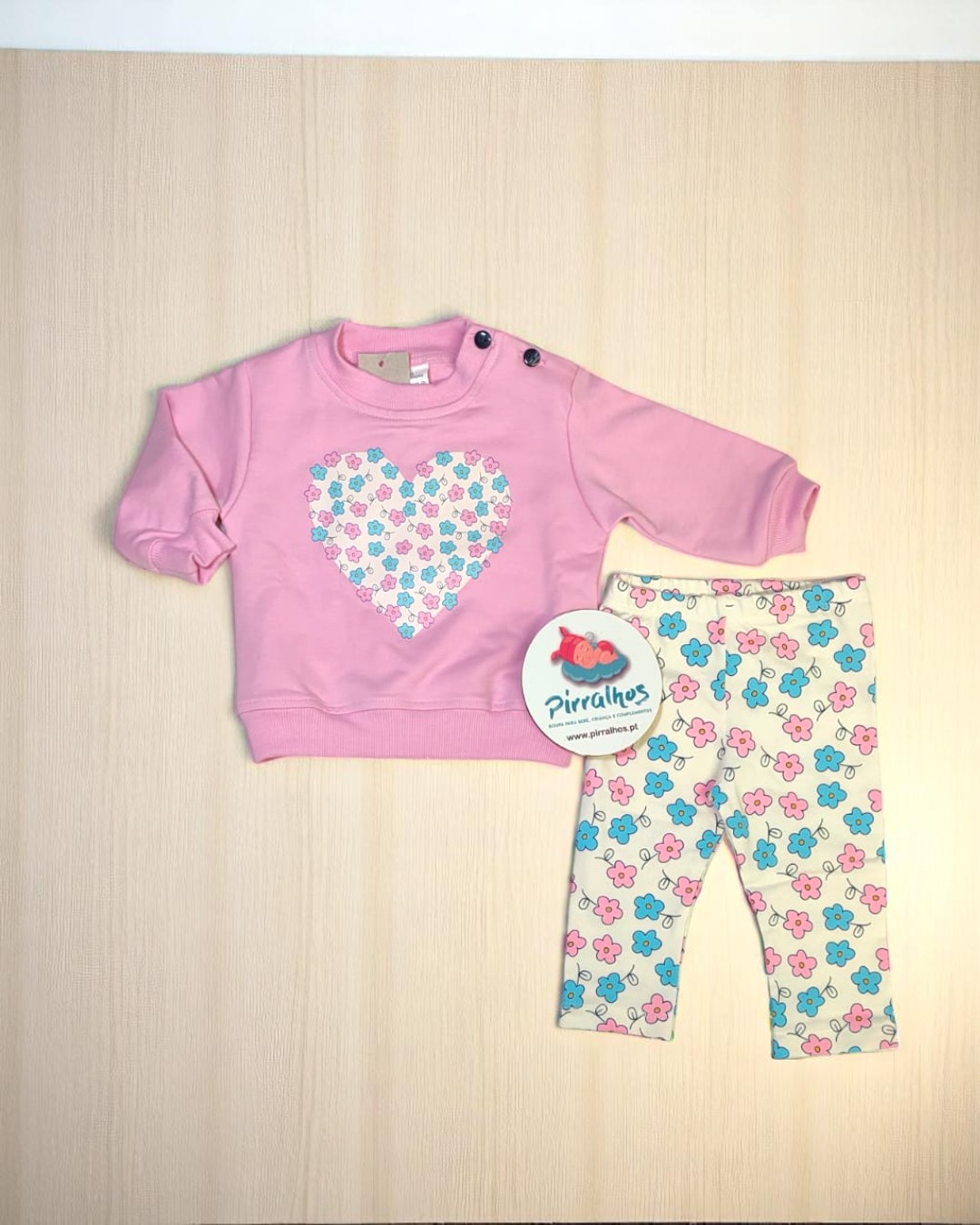 Conjunto de roupa para bebé rosa e branco com padrão de flores.