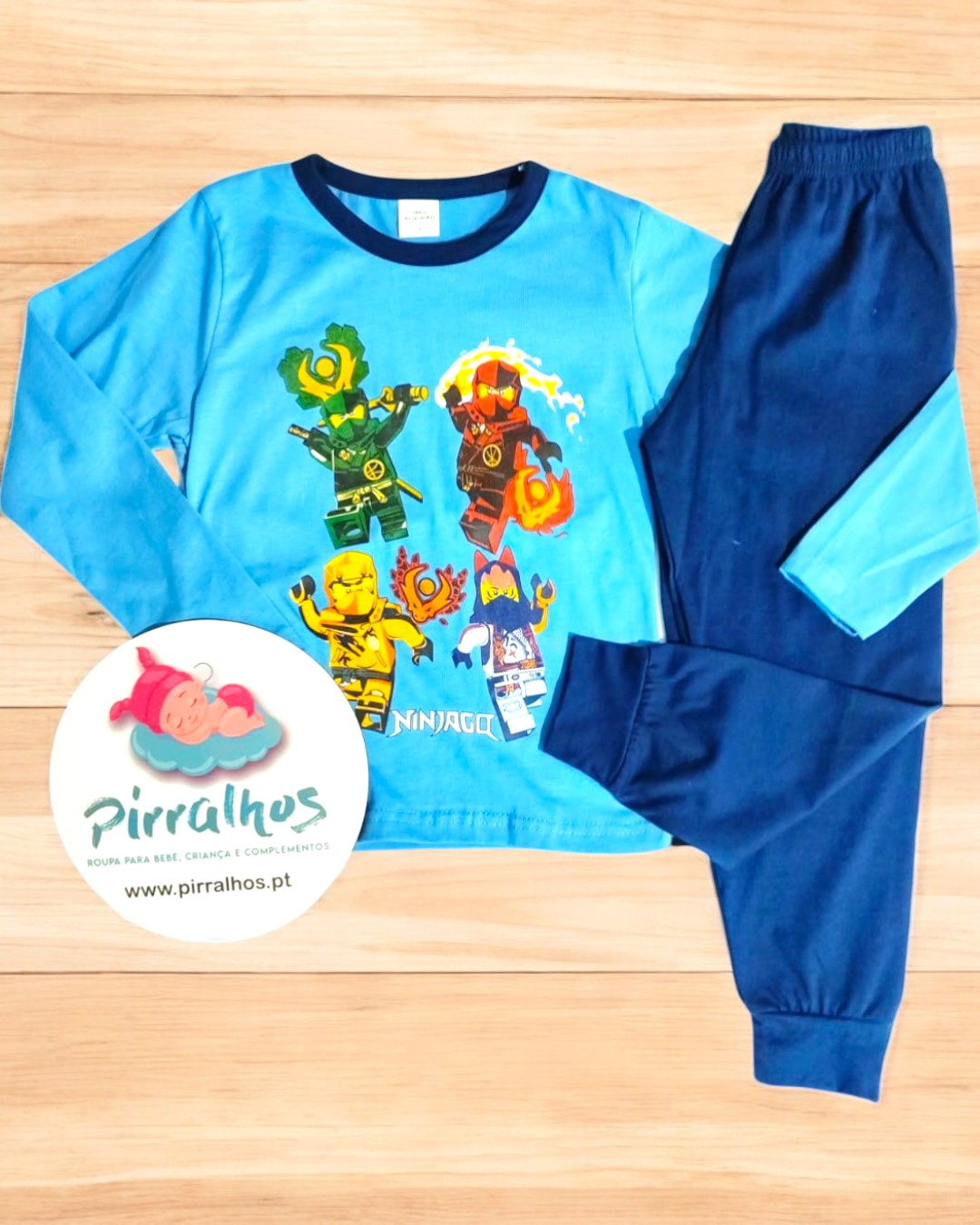 Pijama infantil azul com estampa NINJAGO e calças azuis escuras num fundo de madeira clara