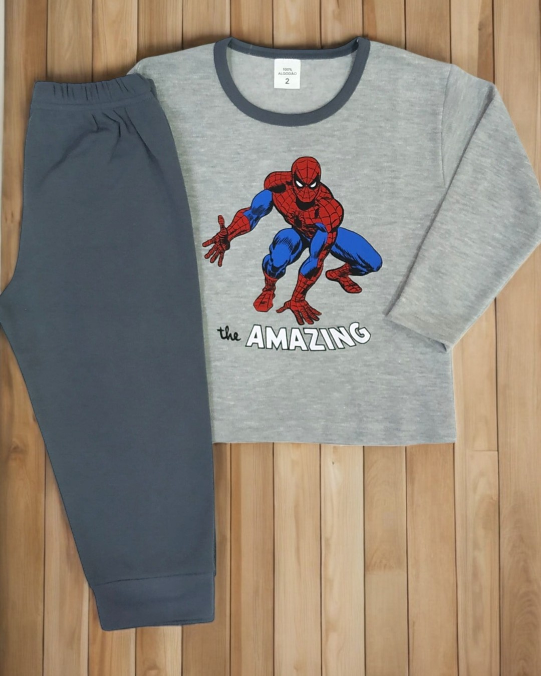 Pijama infantil cinzento com estampa do Homem-Aranha e calças azul escuras sobre chão de madeira