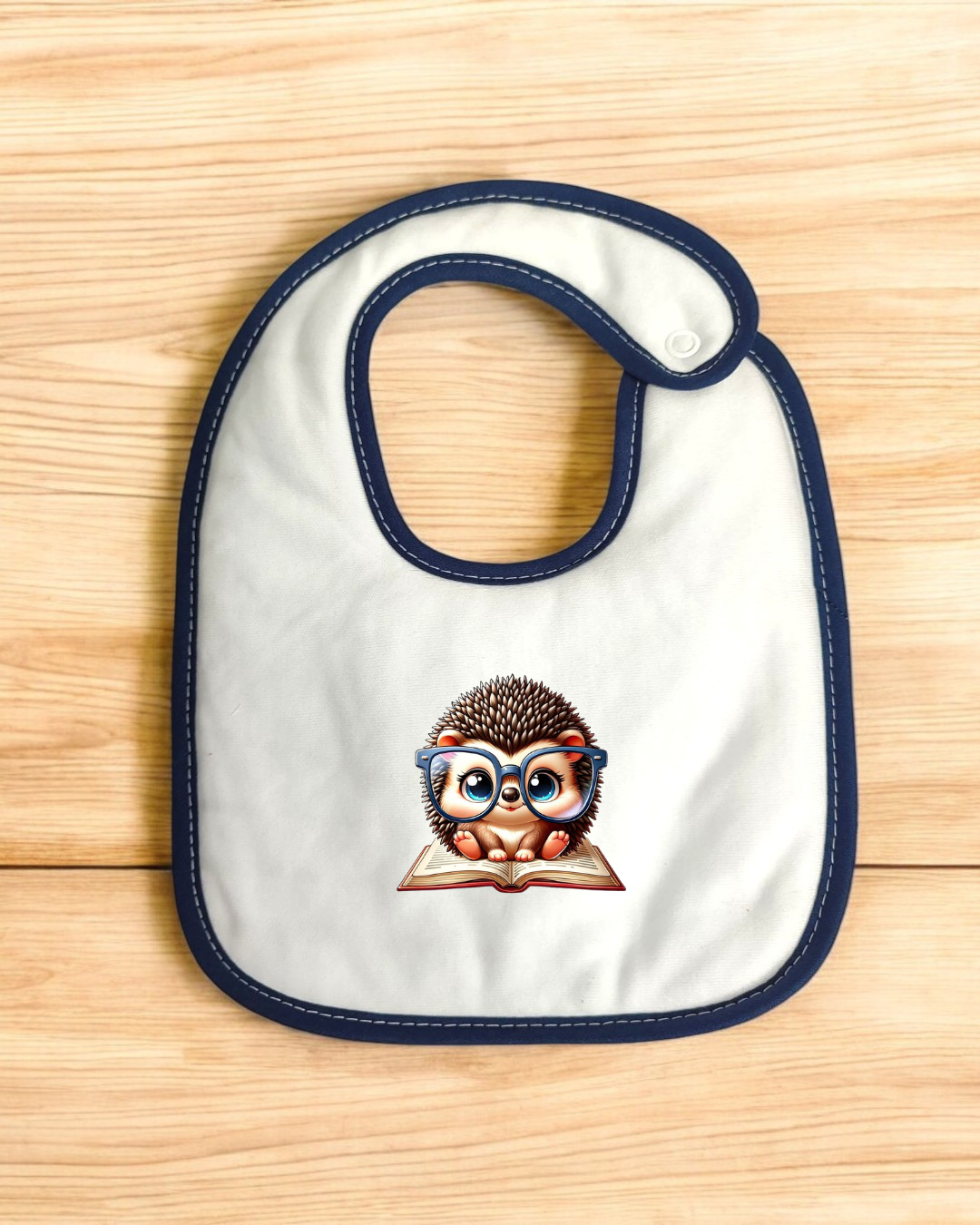Babete branco com bordas azuis e ilustração de ouriço a ler um livro