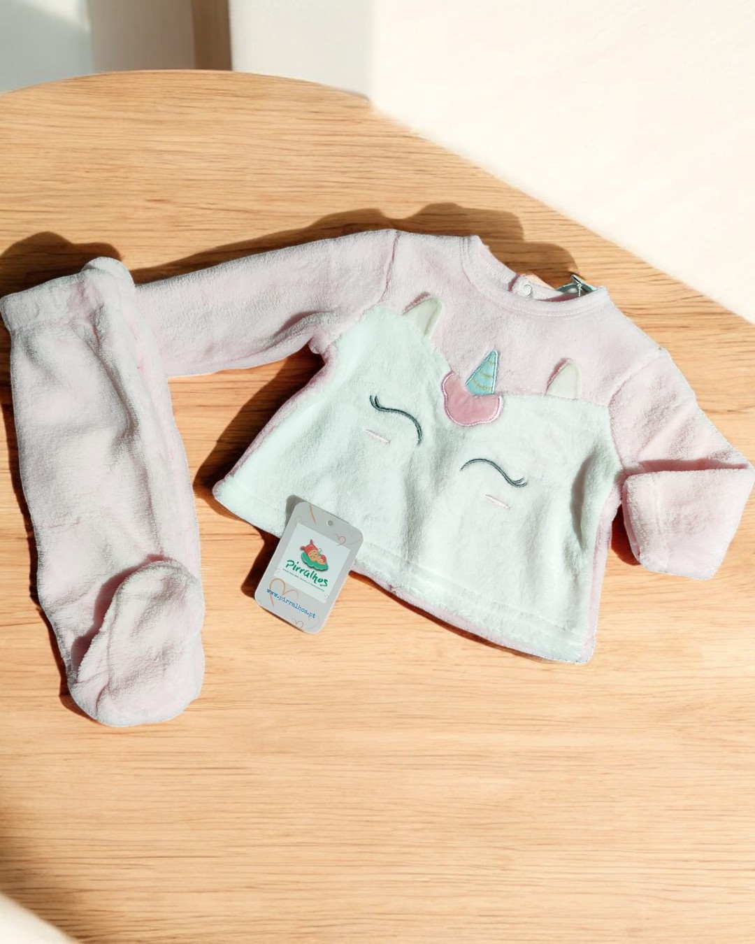 Conjunto bebé rosa unicórnio em tecido felpudo sobre mesa de madeira