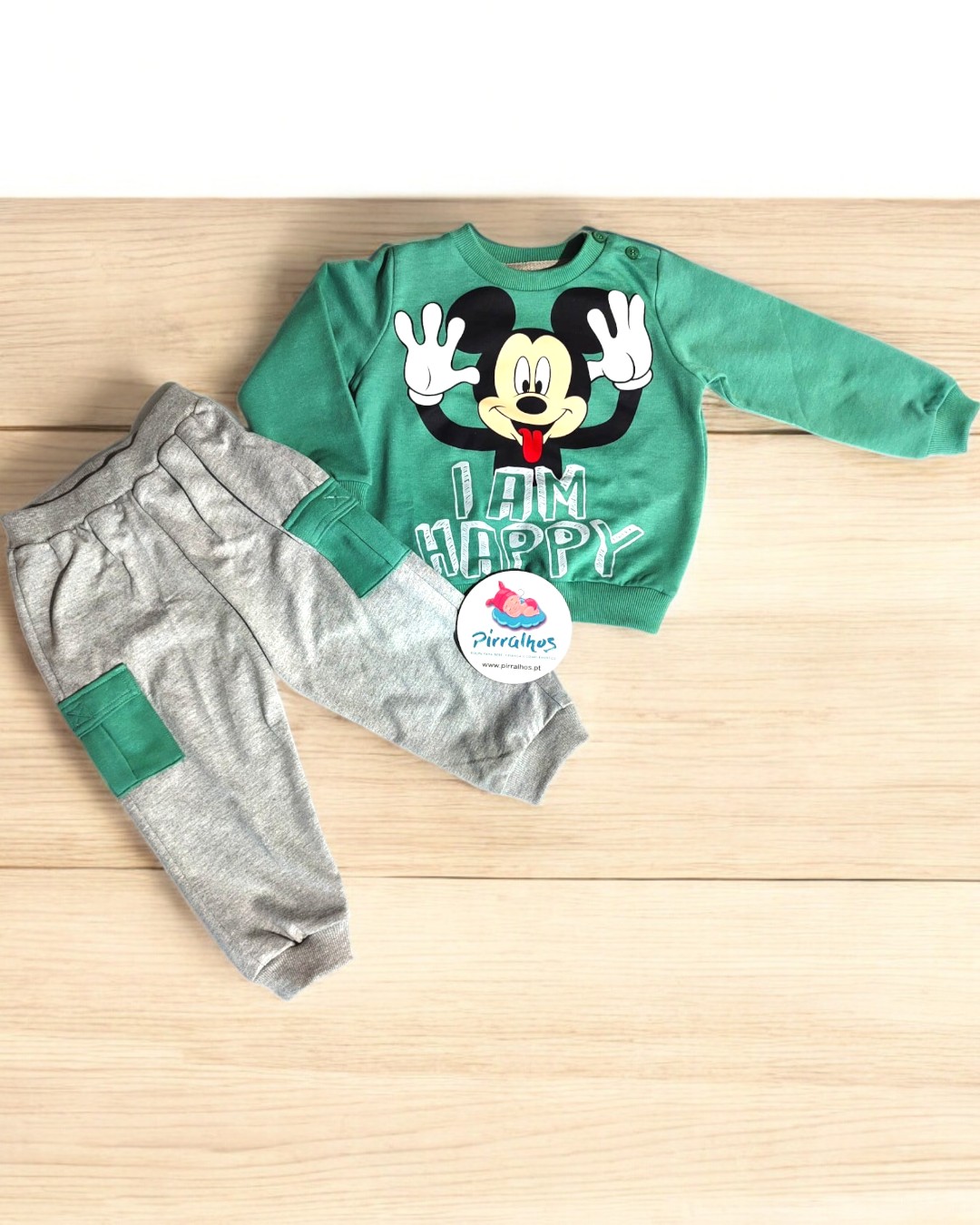 Conjunto de roupa infantil com camisola verde e calças cinzentas, estampa do Mickey e etiqueta da marca.