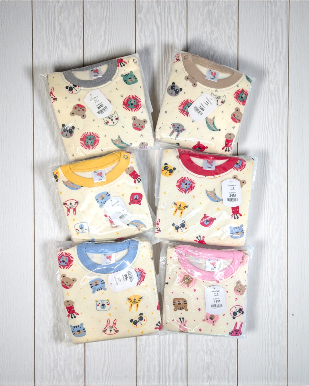 Fatos de bebé dobrados em plástico com estampado de animais e várias golas coloridas em chão de madeira branca