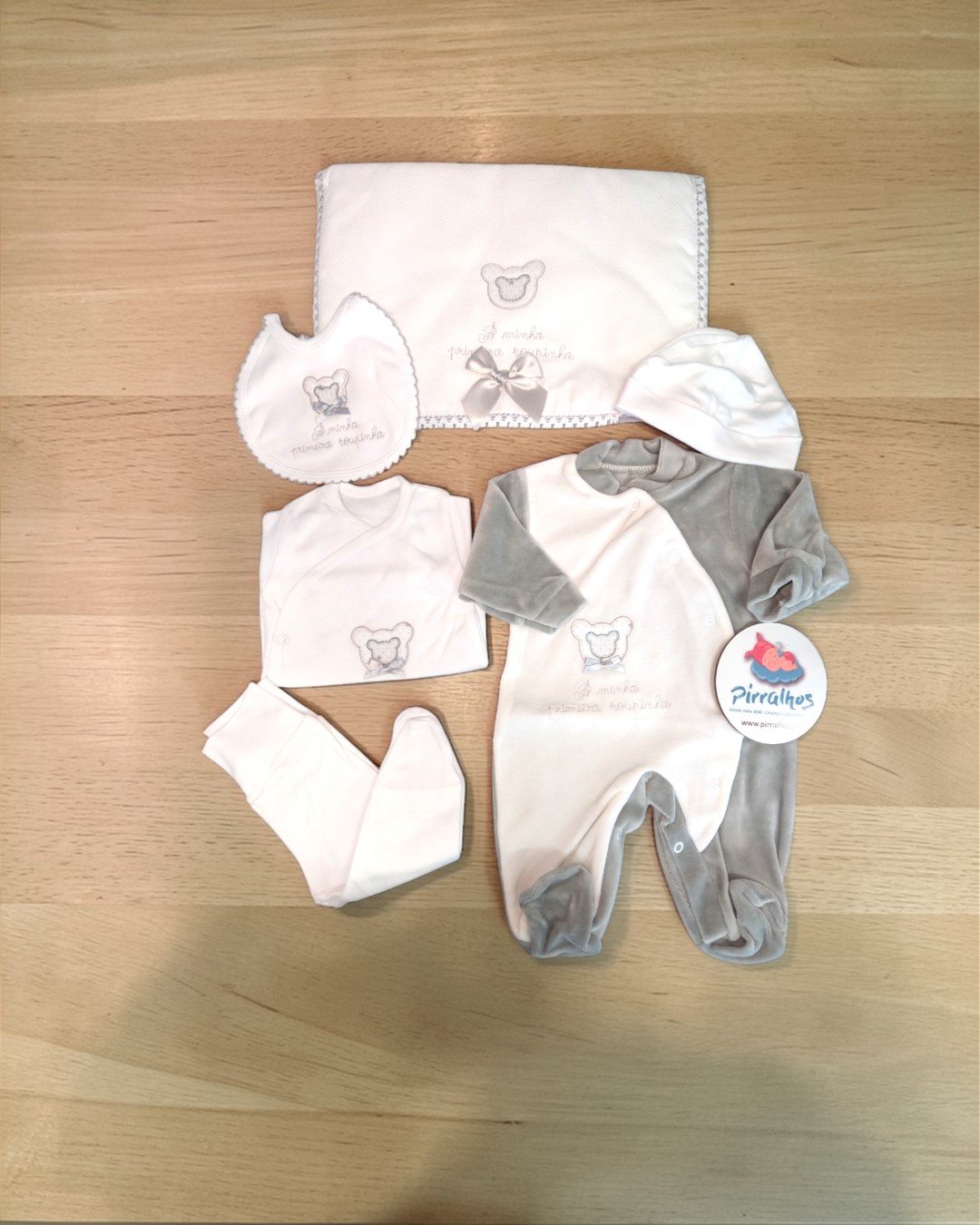 Conjunto de roupa de bebé em branco e cinzento com ursinho e texto A minha primeira roupinha.