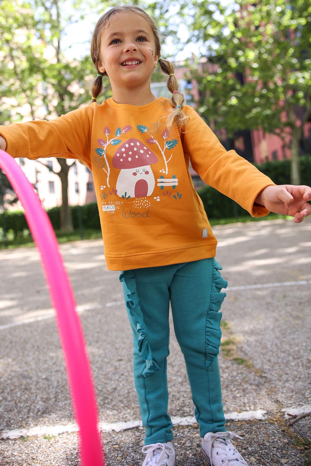 Criança com camisola laranja e calças azuis jogando em parque exterior