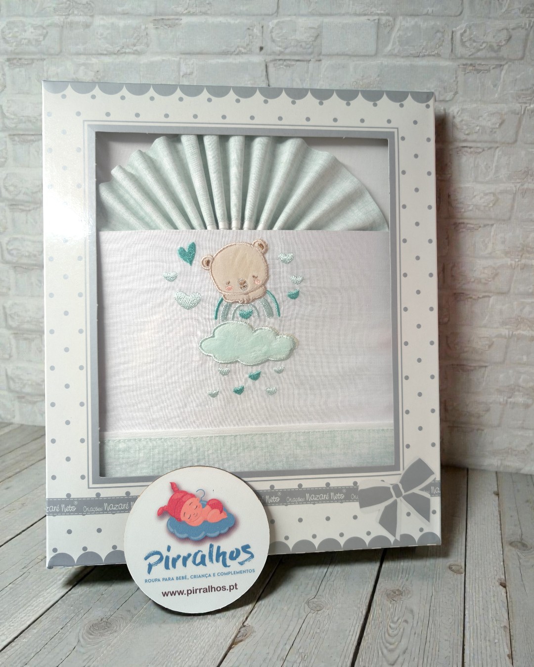 Conjunto de roupa de bebé com bordado de urso numa caixa decorada