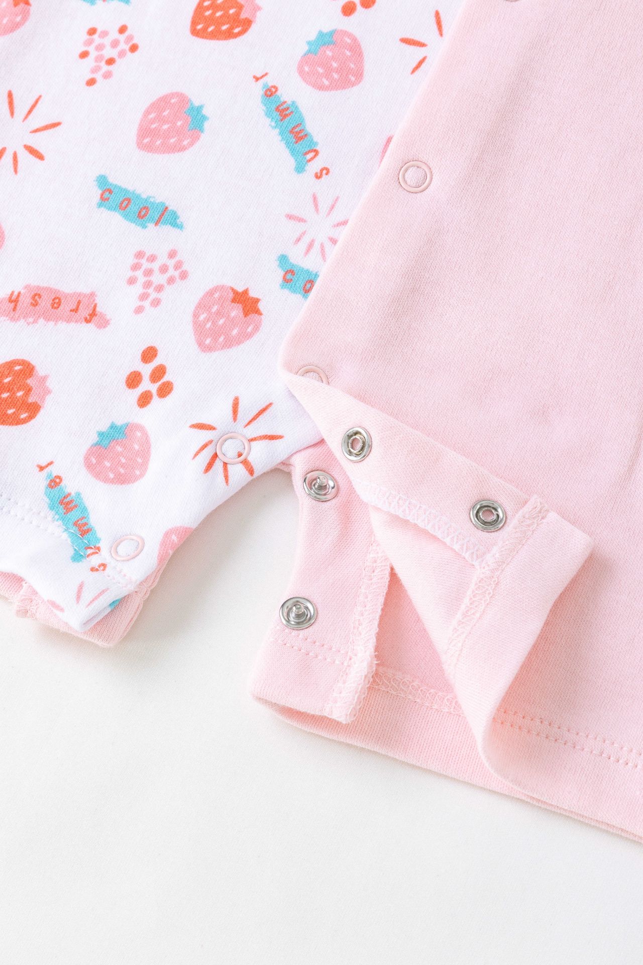 Roupa de bebé com padrão de morangos e roupa cor-de-rosa com fechos de pressão