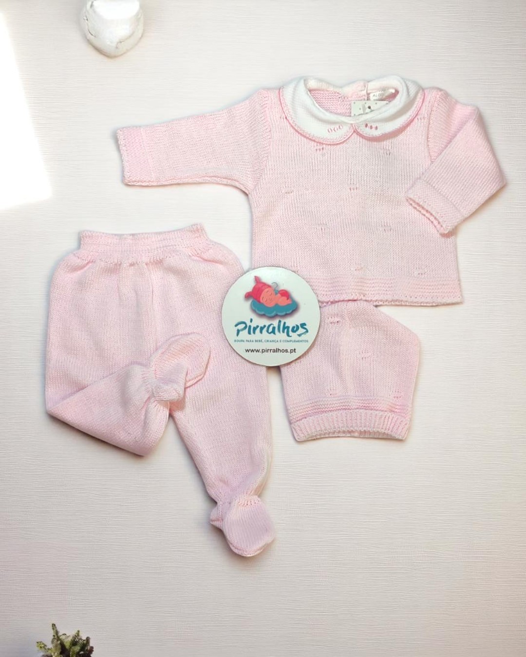 Conjunto de roupa de bebé cor-de-rosa com camisola, calças e gorro, sobre fundo branco