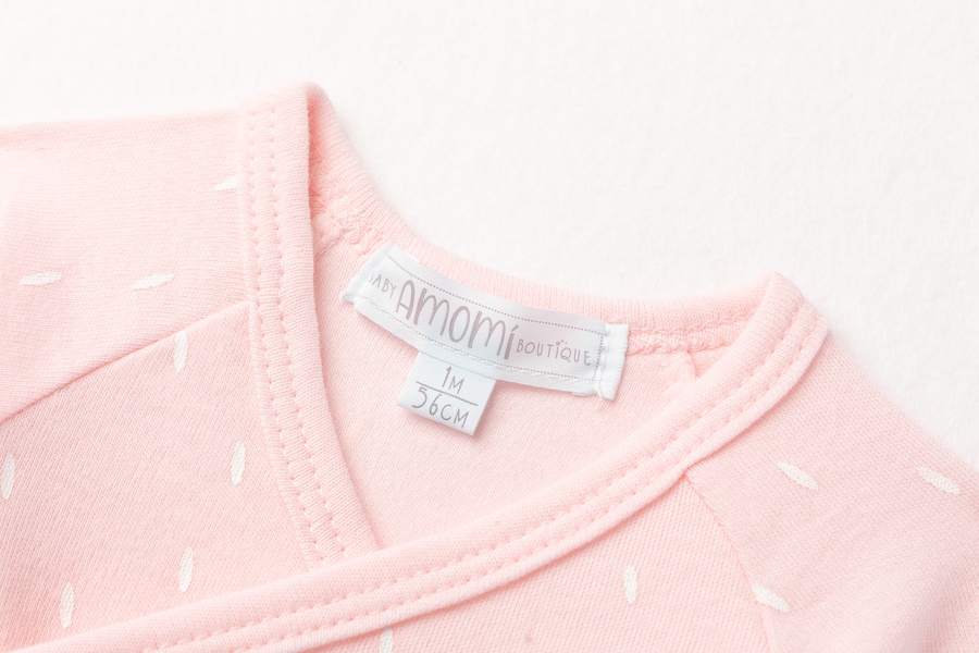 Roupa de bebé rosa com padrão branco e etiqueta amomi