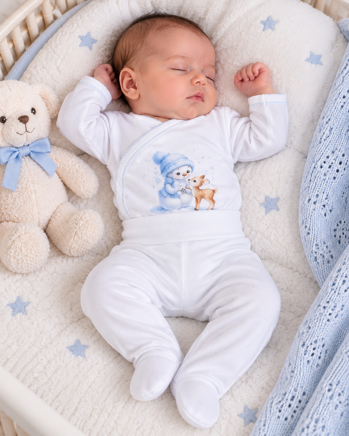 Bebé a dormir com pijama branco estampado e ursinho de peluche num berço acolchoado.
