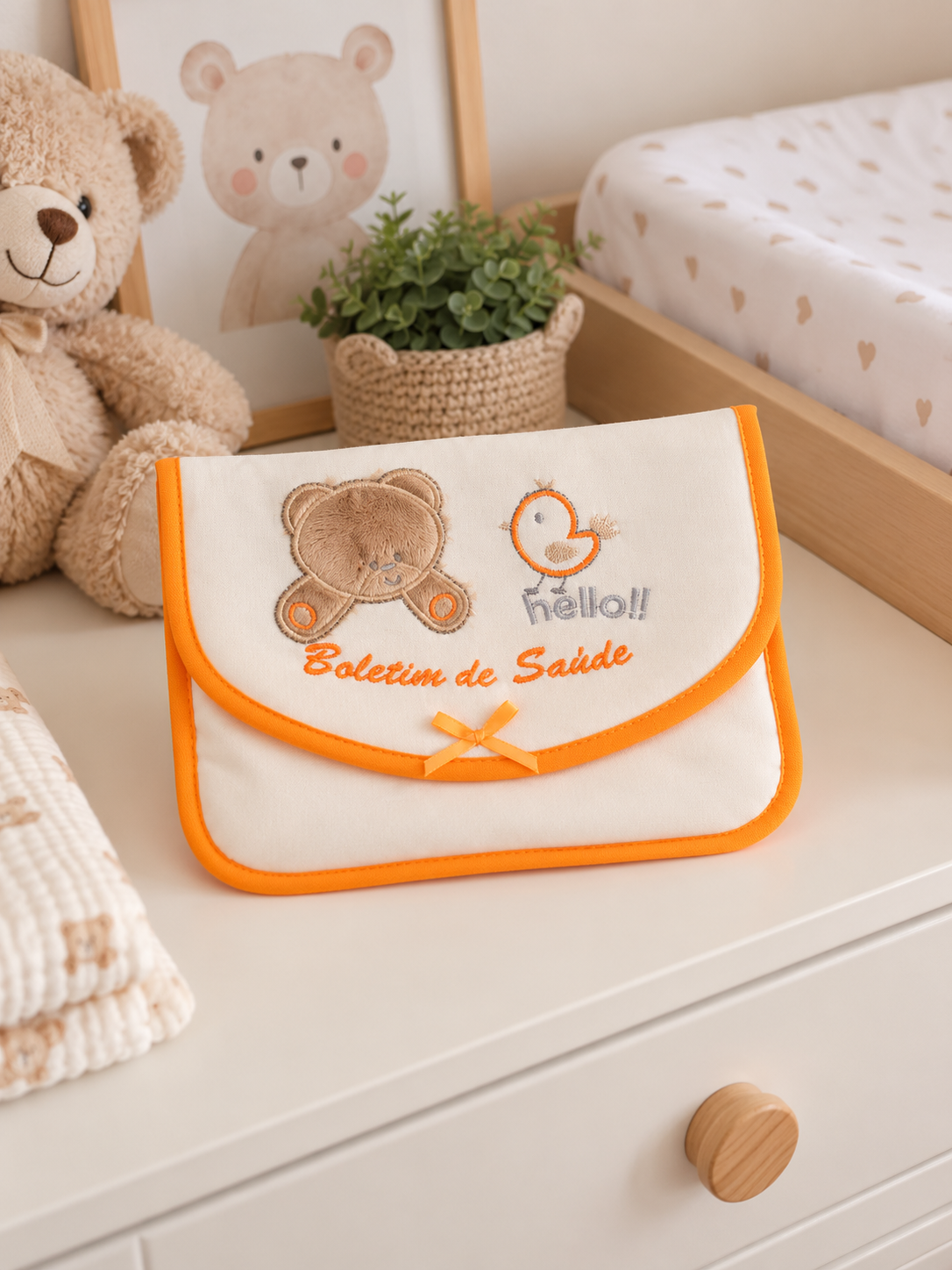 Bolsa creme com bordas laranja e bordados de ursinho e pássaro, texto Boletim de Saúde sobre cómoda branca num quarto de criança
