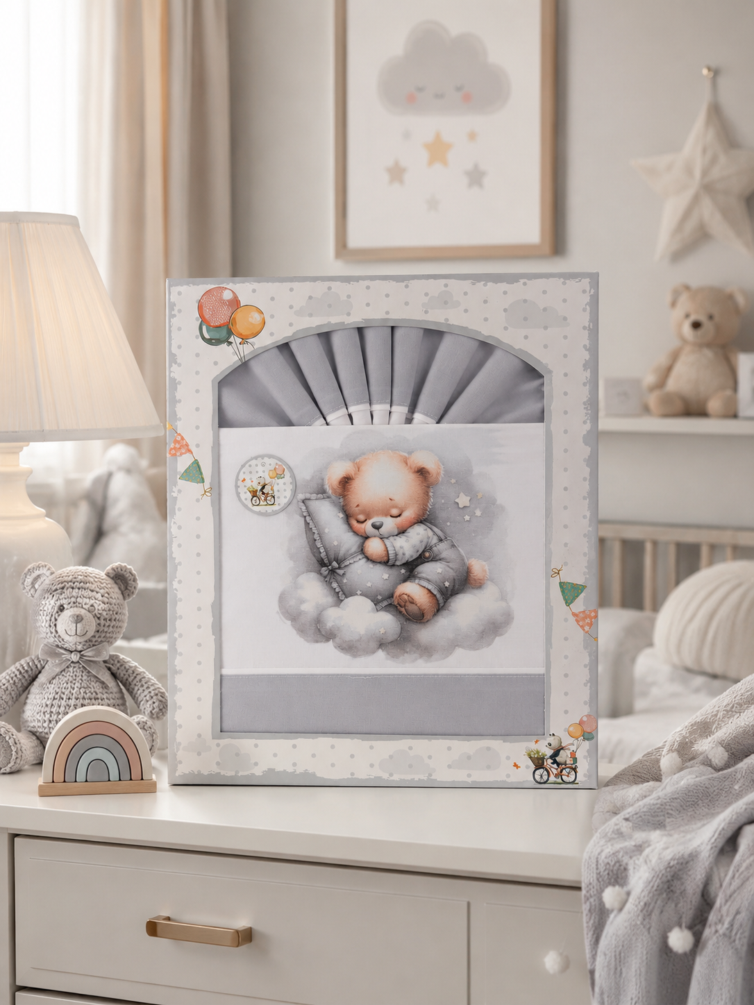 Caixa com roupa de bebé azul e ursinho a dormir embalada, sobre uma cómoda com decoração infantil.