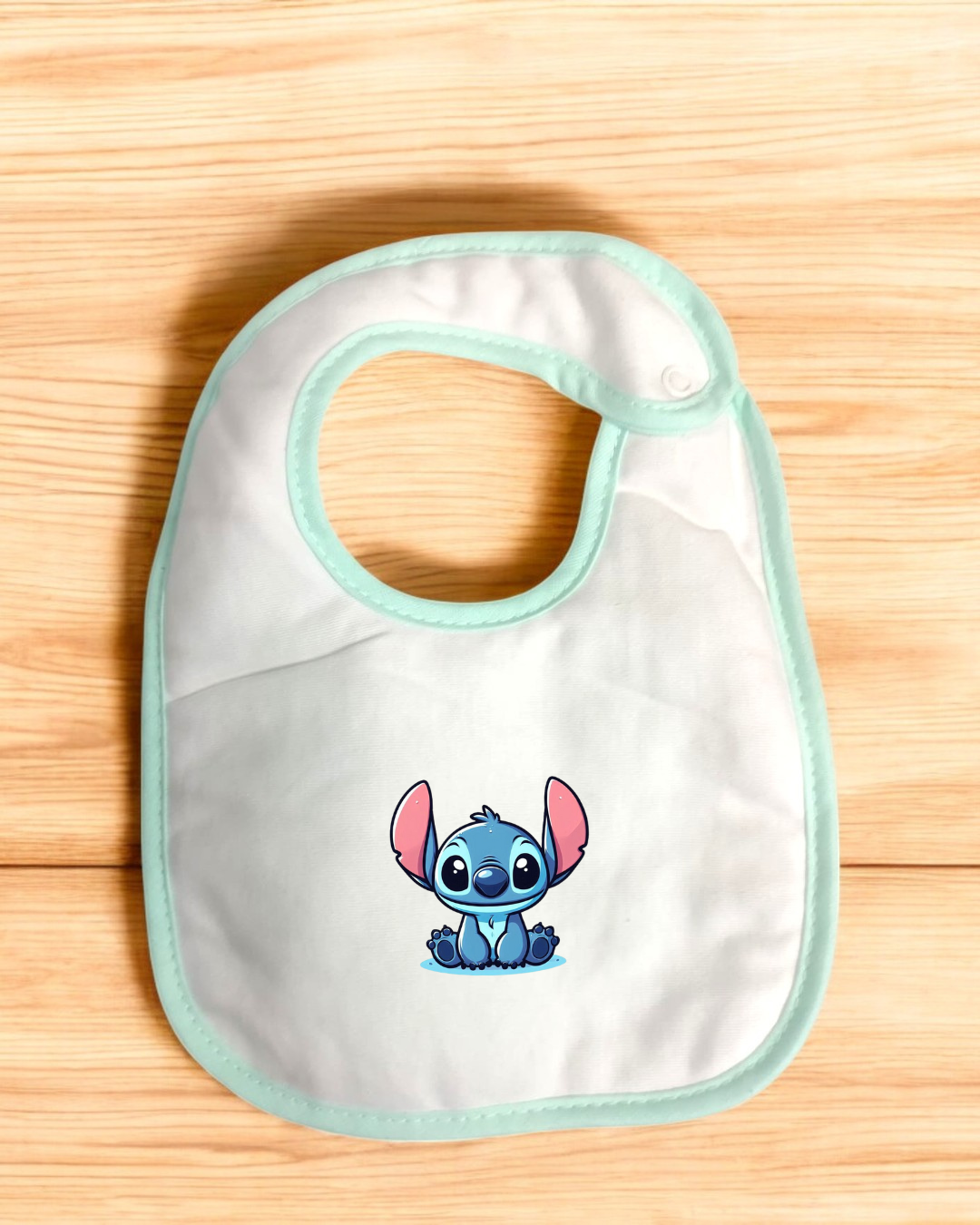 Babete branco com borda verde água e personagem azul com orelhas cor-de-rosa