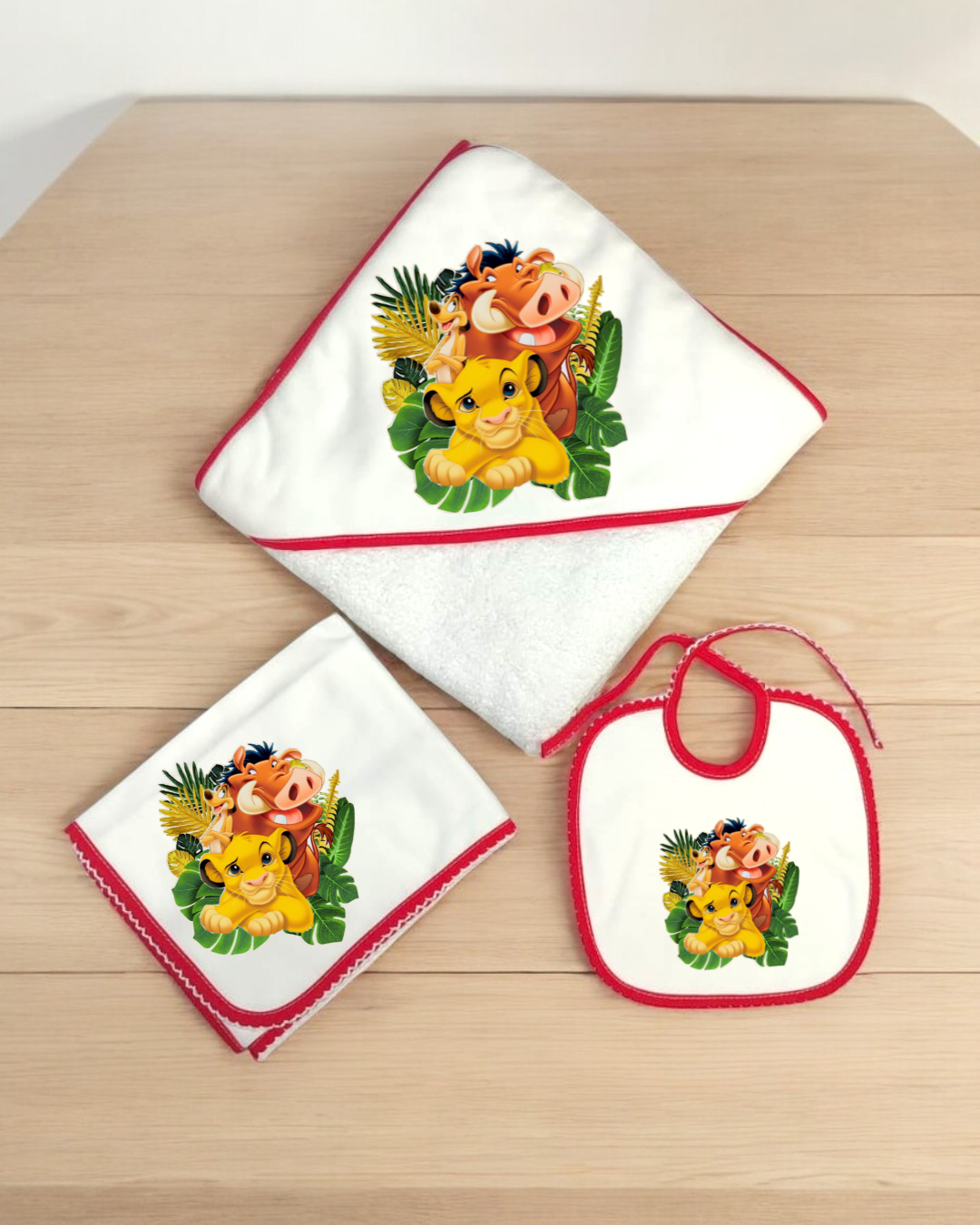 Conjunto de toalha com capuz, babete e fralda branco com bordas vermelhas e estampa dos personagens Timão, Pumba e Simba de O Rei Leão
