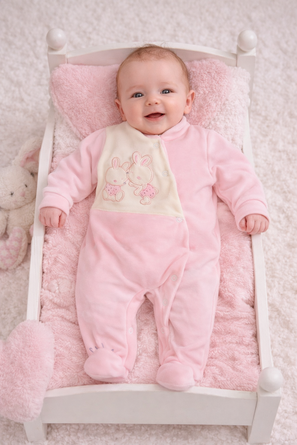 Bebé deitado numa cama branca com pijama rosa e bordado de coelhinhos
