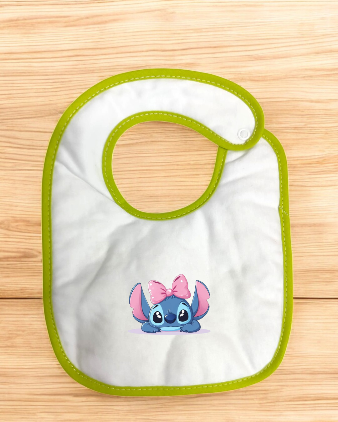 Babete branco com bordas verdes e personagem azul com laço rosa