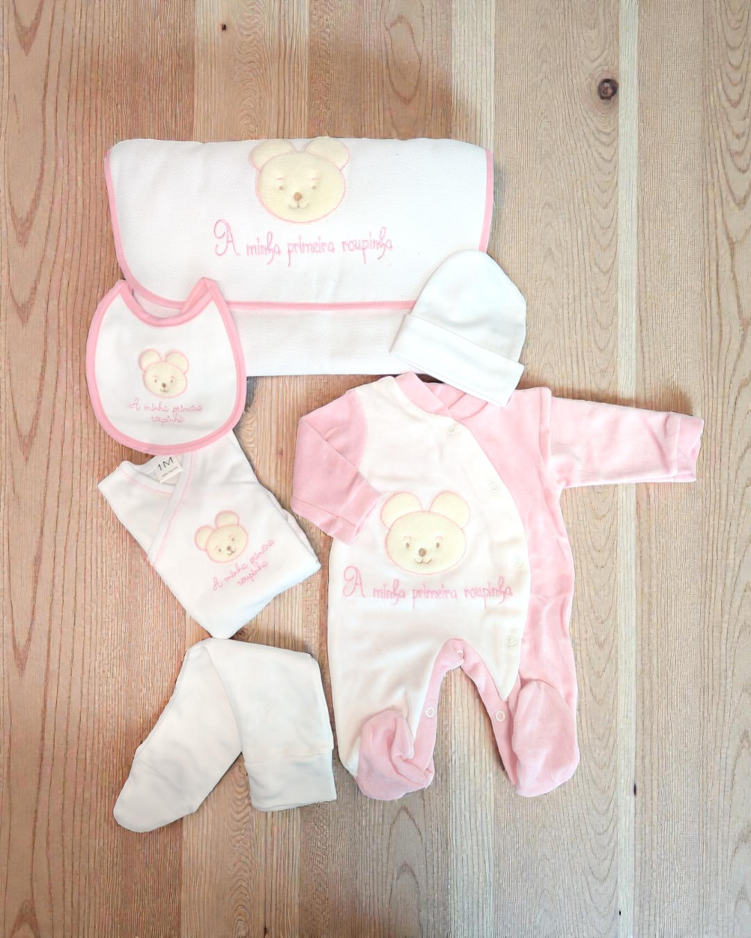 Conjunto rosa e branco de roupa de bebé com ursinho bordado e texto
