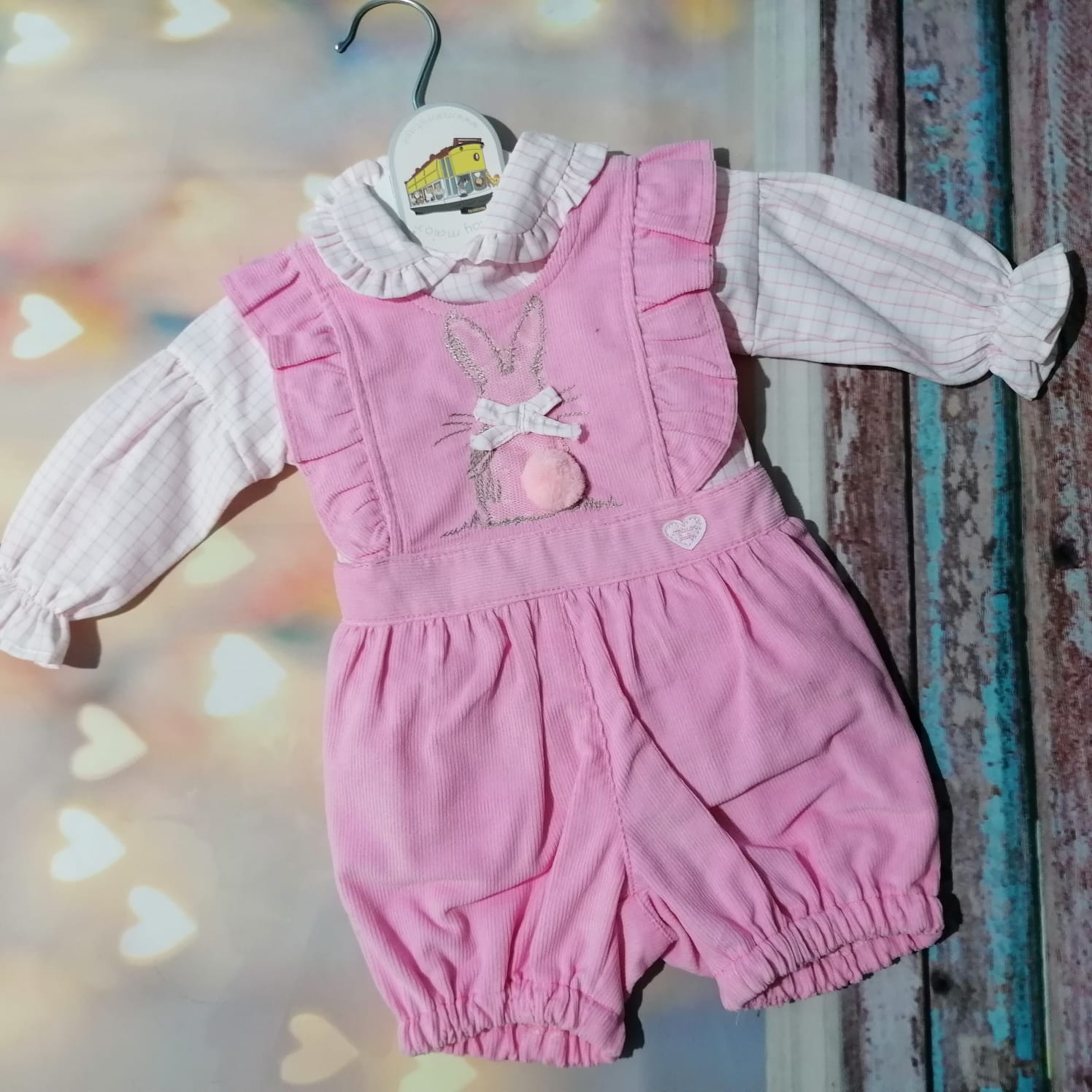 Roupa de bebé rosa e creme pendurada num cabide branco