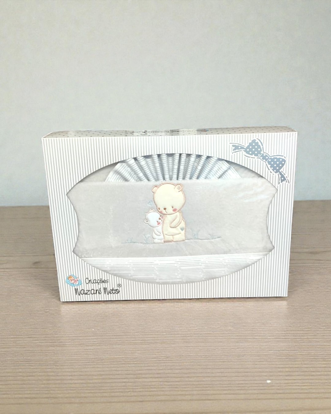 Caixa branca com riscas cinzentas contendo uma manta com bordado de ursos e laço azul na embalagem
