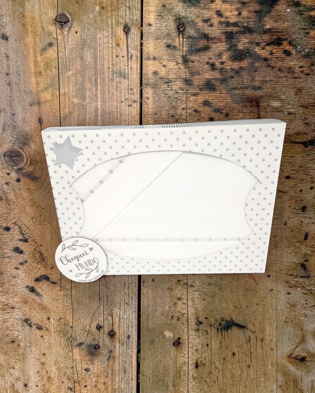 Caixa decorativa com conjunto branco de lençóis ou fraldas com bordado e fita, sobre fundo de madeira rústica