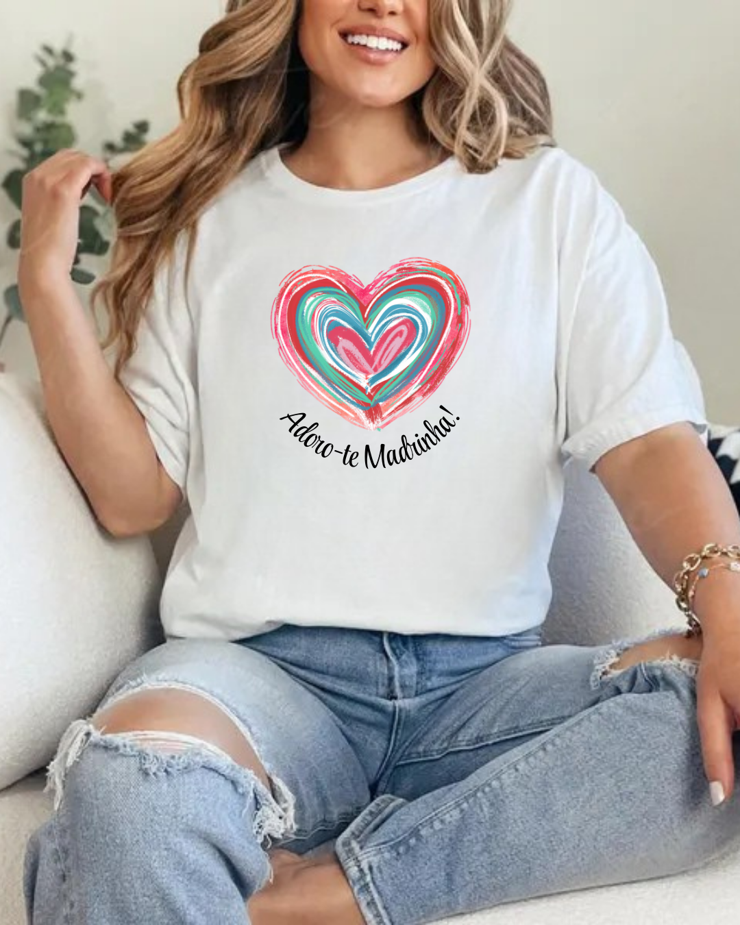 Mulher sentada com t-shirt branca estampada com coração colorido e texto em português.