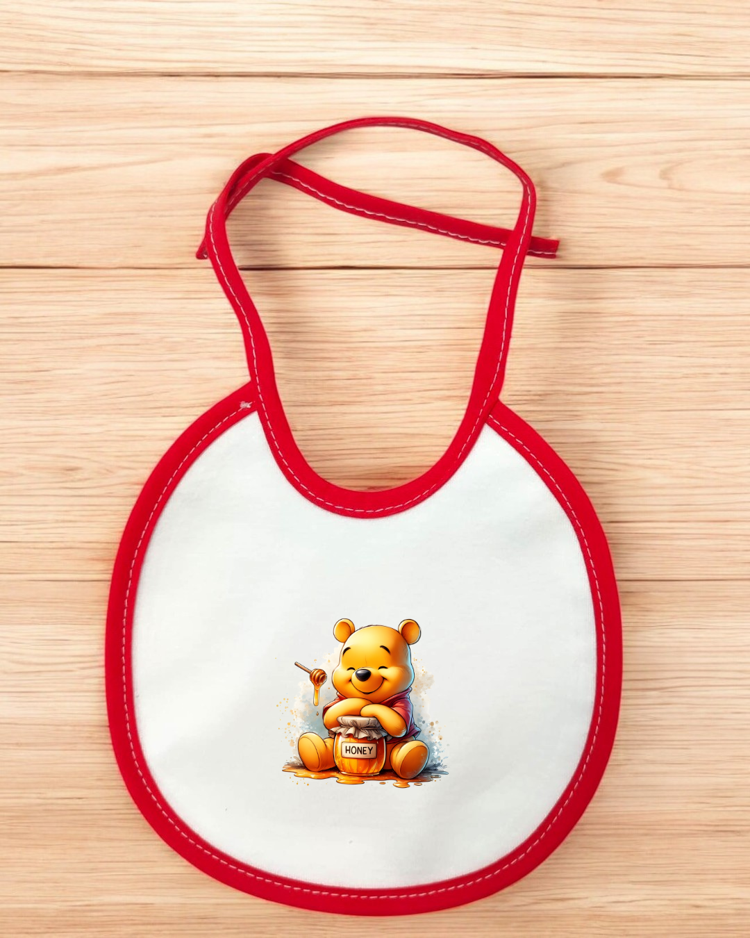 Babete branco com borda vermelha e desenho do Ursinho Pooh com pote de mel