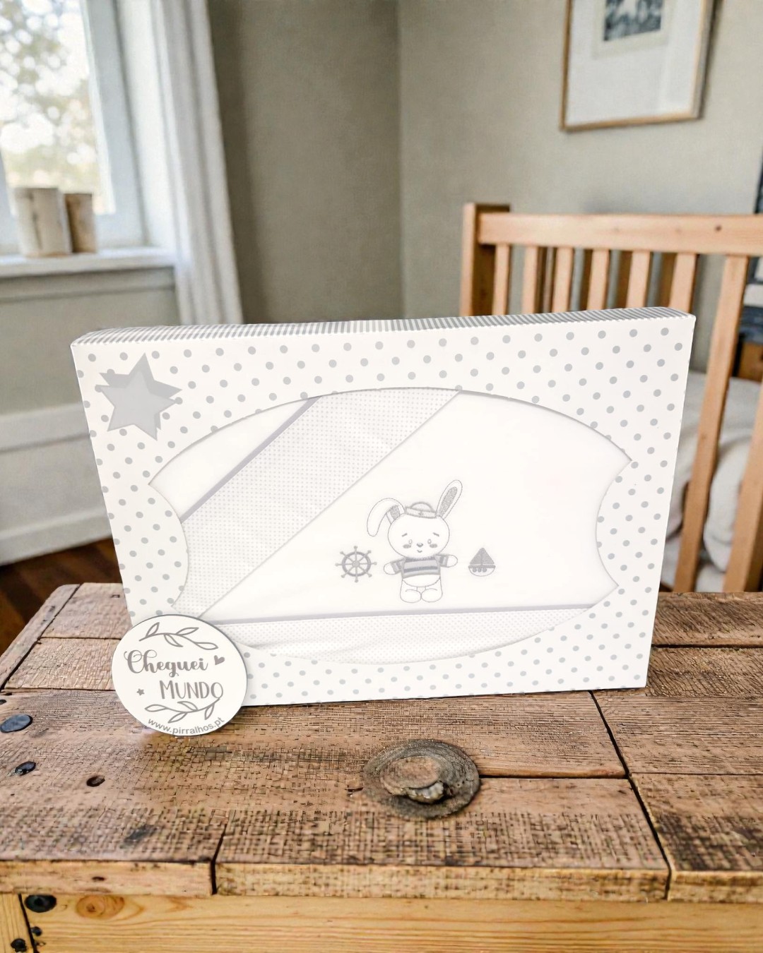 Embalagem de conjunto de roupa de bebê com desenho de coelho, timão e barco, em mesa de madeira.