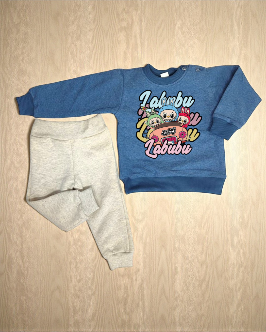 Conjunto infantil azul com estampado e calças cinza claras sobre madeira clara