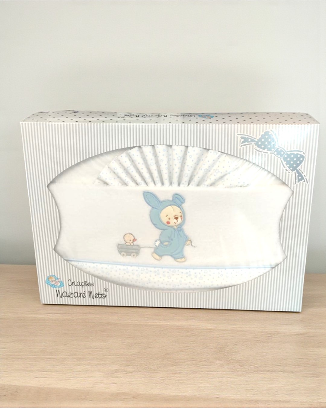 Conjunto de roupa de bebé branca com desenho azul embalada em caixa branca listrada
