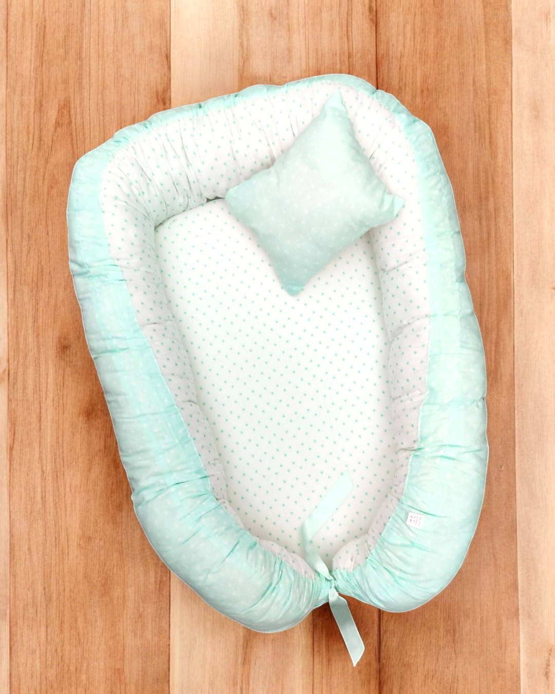 Ninho de bebé azul claro com almofada sobre chão de madeira